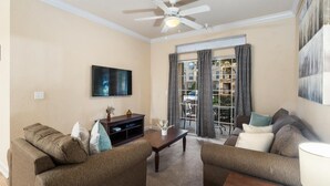 A living room with a ceiling fan, a flat-screen TV, two couches, a coffee table, and a window with curtains. - Tuscana Resort 2 Bedroom Condo Clubhouse Access 8 miles to Disney 2 Condo (Davenport)