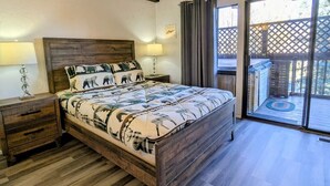 A bedroom with a wooden bed, two bedside tables, and a view of a deck through a glass door. - Charming Forest Retreat – Steps from Snow Summit Slopes (Big Bear Lake)