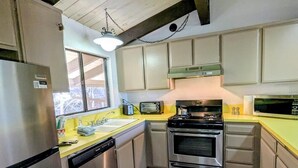 A kitchen with stainless steel appliances, a yellow countertop, and a window providing natural light. - Charming Forest Retreat – Steps from Snow Summit Slopes (Big Bear Lake)