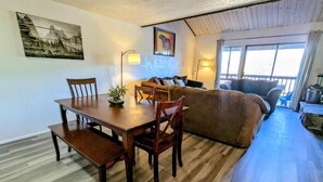 A cozy room with a wooden dining table, chairs, a sofa, and a couch. There are two paintings on the walls and a window with curtains. - Charming Forest Retreat – Steps from Snow Summit Slopes (Big Bear Lake)