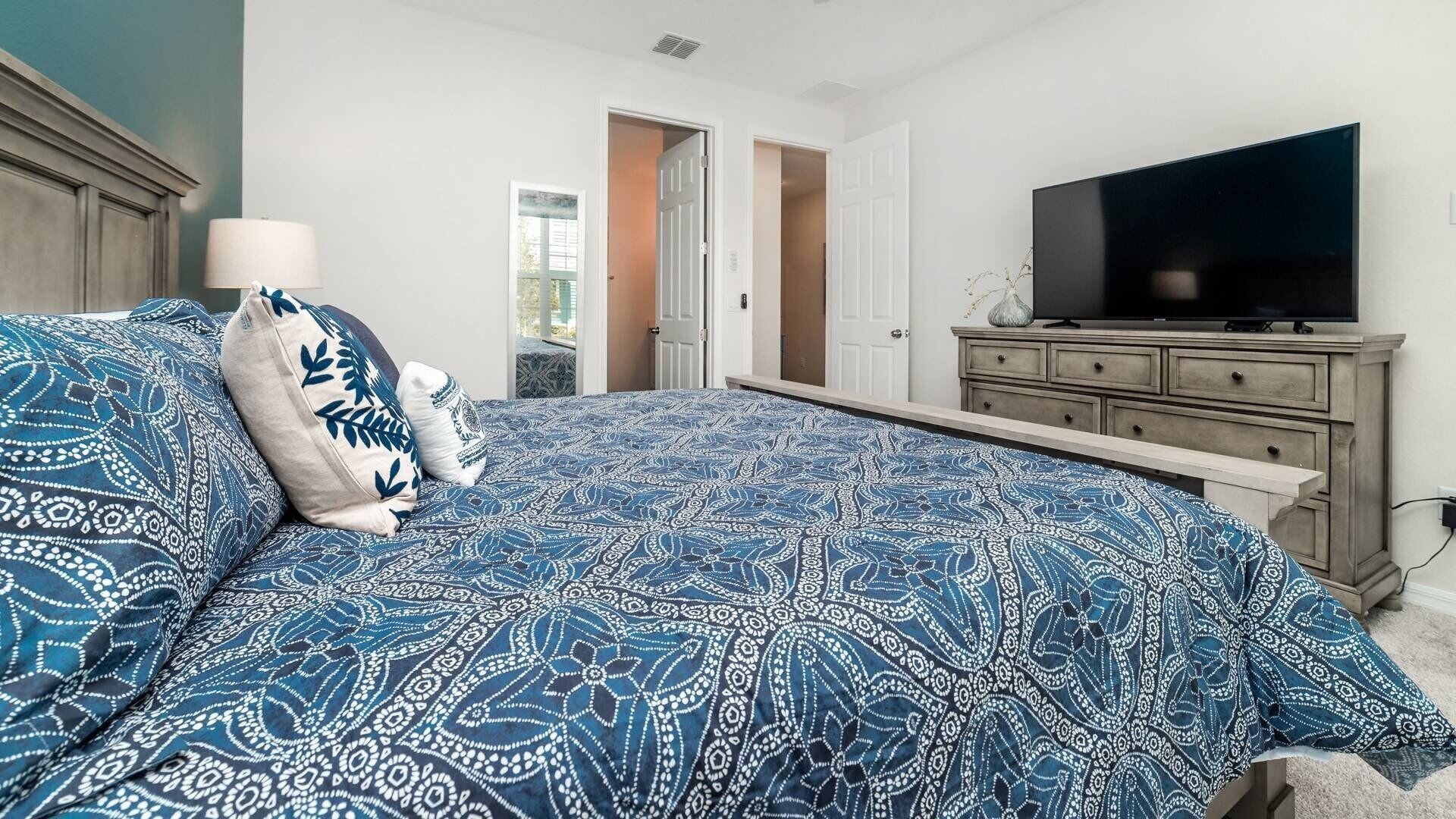 Une chambre avec un grand lit, un téléviseur posé sur une commode et une porte donnant sur une autre pièce.