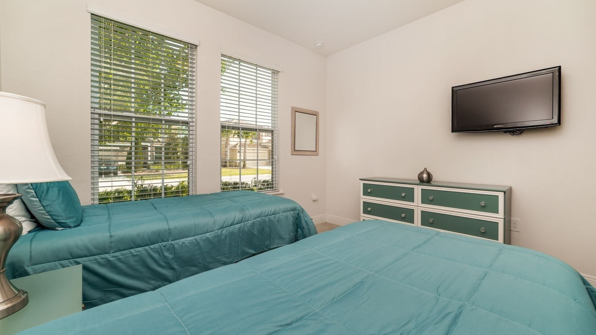 A bedroom with two beds, a dresser, a TV, and windows with blinds.
