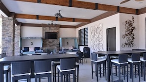 An outdoor dining area with a stone wall, a flat-screen TV, and abstract wall art. - Solterra Resort 5 Bedroom Pool Home Pet Friendly 5 Home (Davenport)