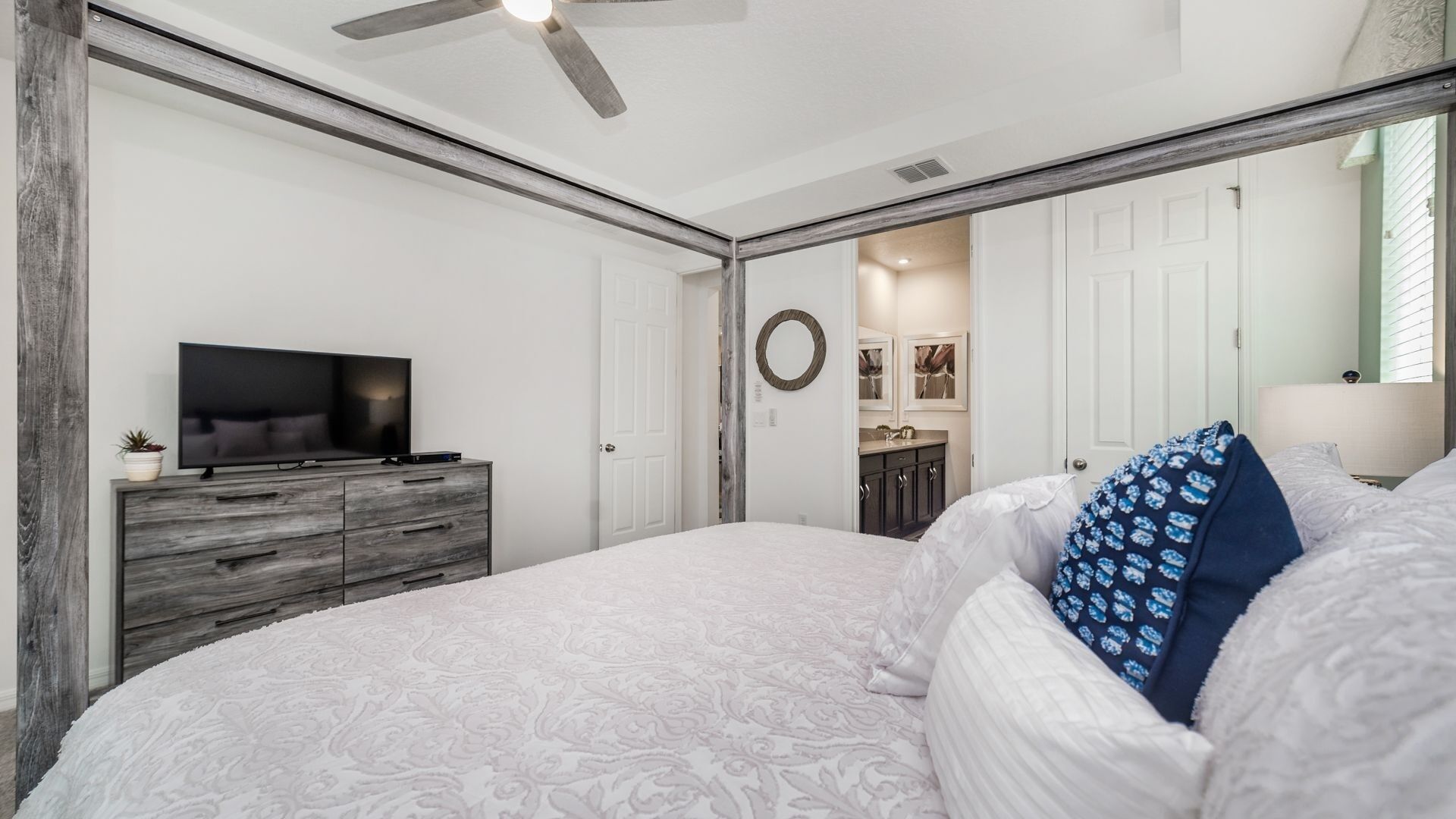 Een slaapkamer met een groot bed, een televisie op een houten dressoir en een spiegel aan de muur.