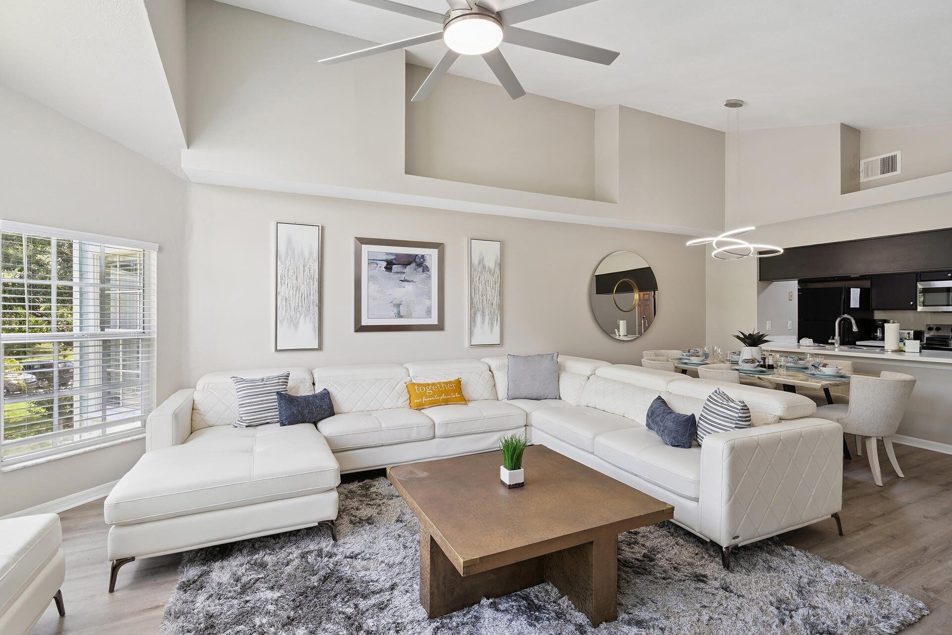 A modern living room with a sectional sofa, a coffee table, and a dining area with a kitchen in the background.