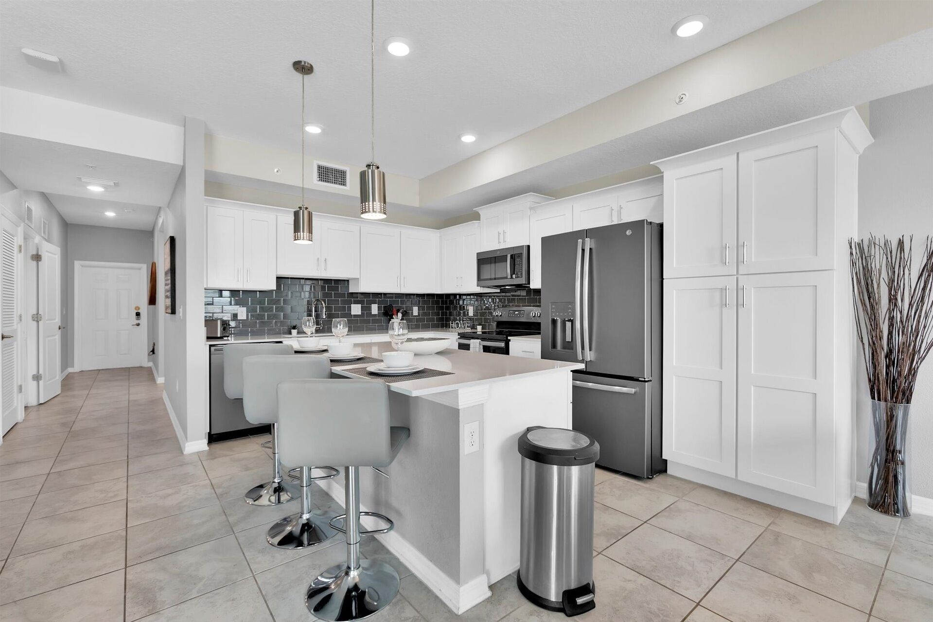 A modern kitchen with white cabinetry, stainless steel appliances, and a central island with bar stools.