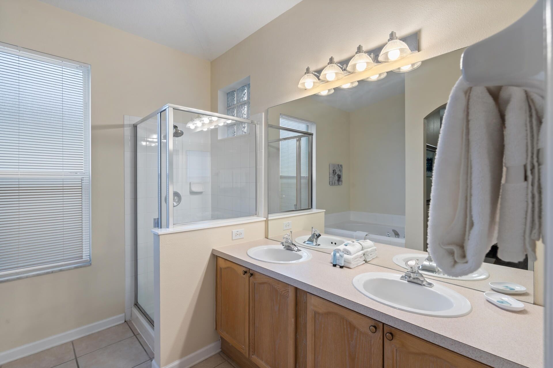 A modern bathroom with two sinks, a glass-enclosed shower, and a large mirror with lights above.