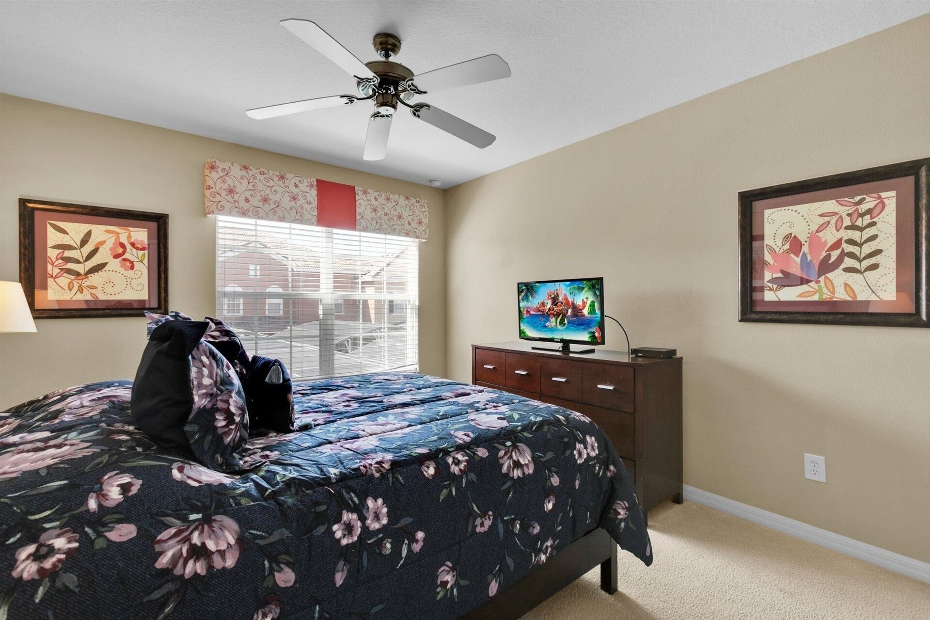 A bedroom with a bed, a ceiling fan, a TV, and artwork on the walls.
