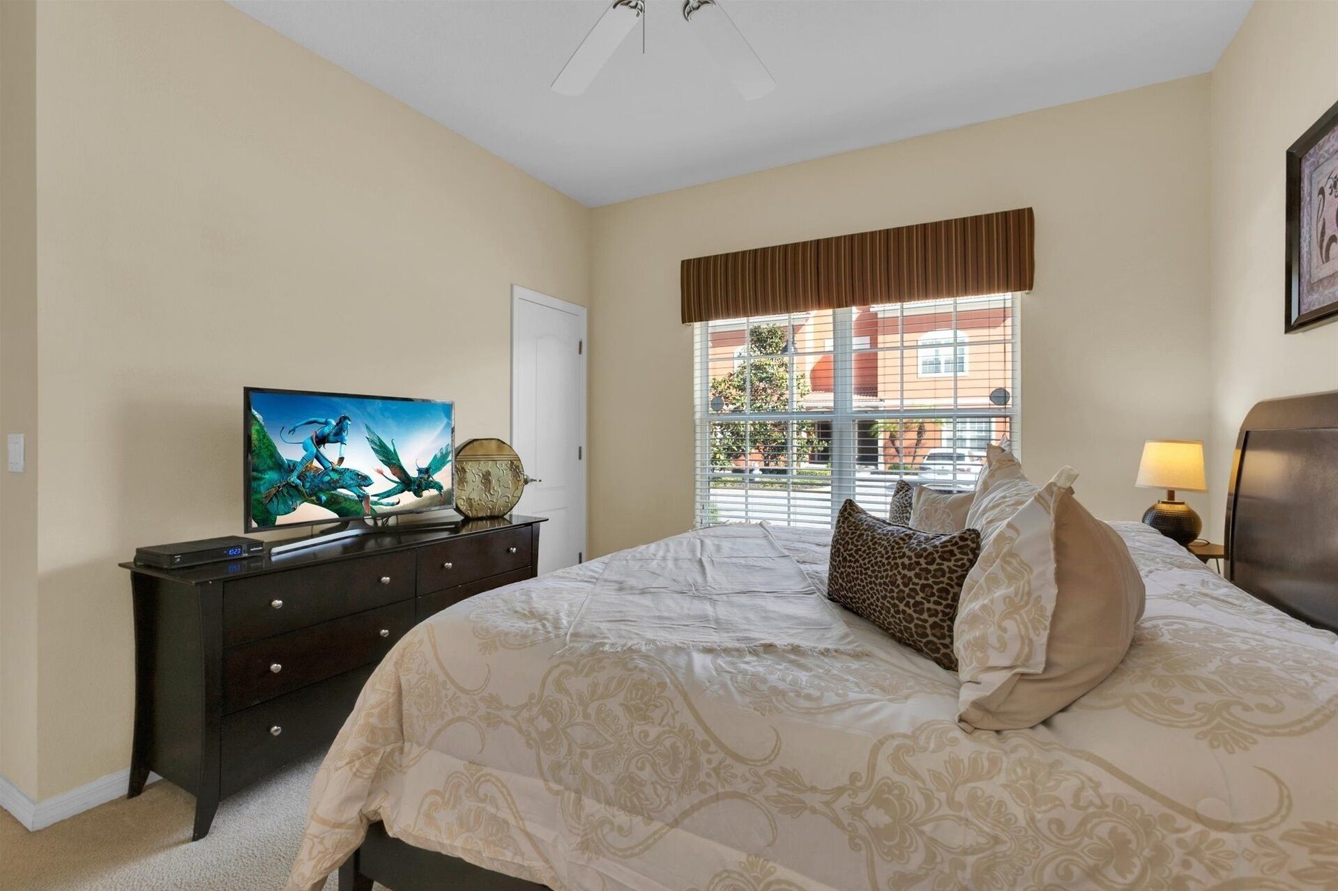 Une chambre à coucher avec un lit, une commode, un téléviseur et une fenêtre avec des stores.