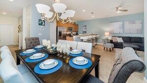A dining area with a dark wooden table set for six, surrounded by white upholstered chairs. - Paradise Palms Resort 4 Bedroom Private Pool Townhome 4 Townhouse (Kissimmee)