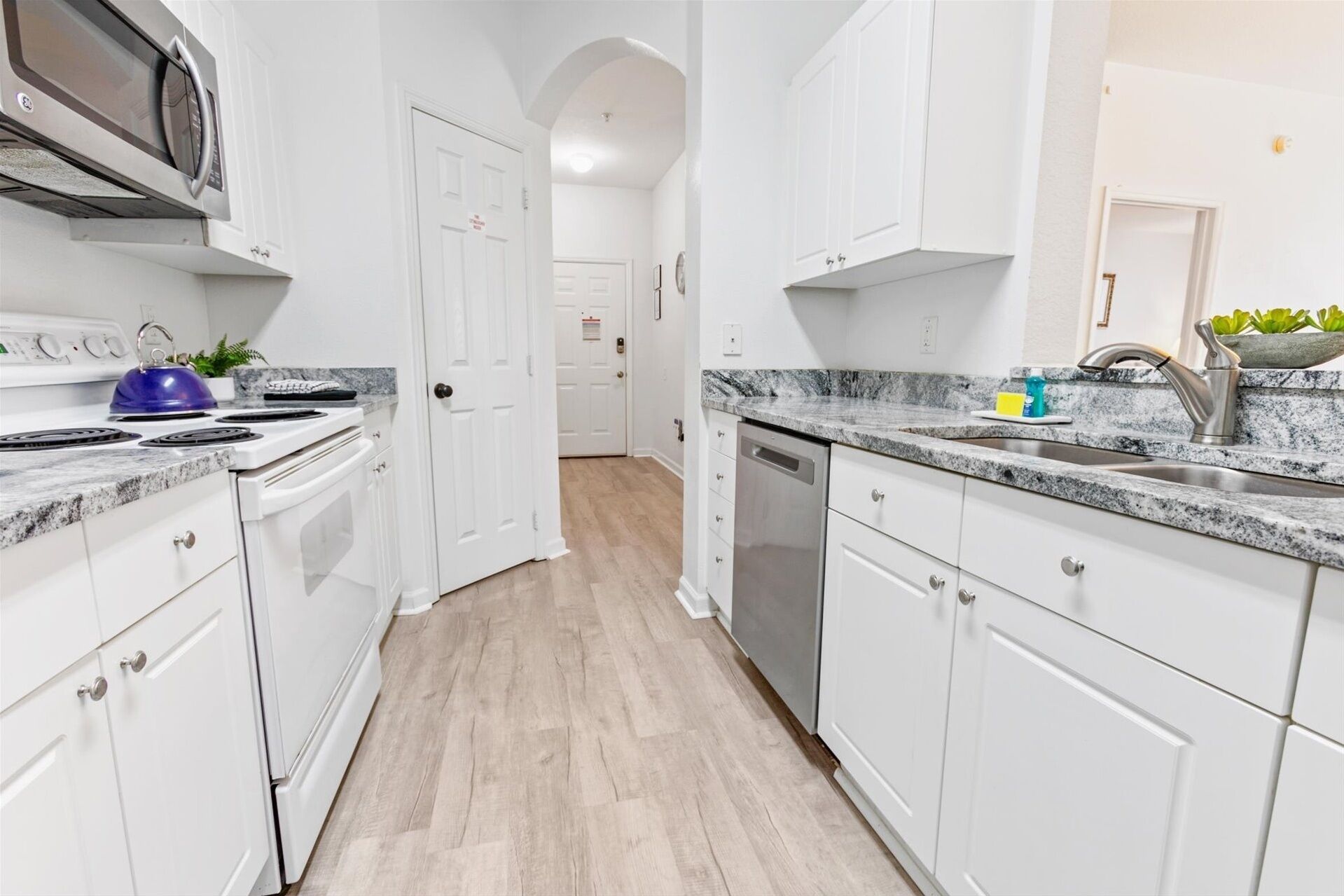 A modern kitchen with white cabinetry, a stainless steel dishwasher, and a granite countertop.