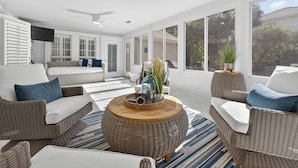 A bright, sunlit room with wicker furniture, a large round coffee table, and a view of the outdoors through large windows. - Private Pool~Sleeps 10~Golf Cart 6 Passenger Included~Walk to beach (Destin)