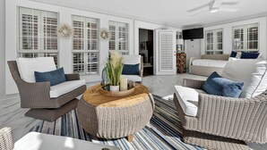A spacious living room with wicker furniture, a round wooden coffee table, and large windows with shutters. - Private Pool~Sleeps 10~Golf Cart 6 Passenger Included~Walk to beach (Destin)