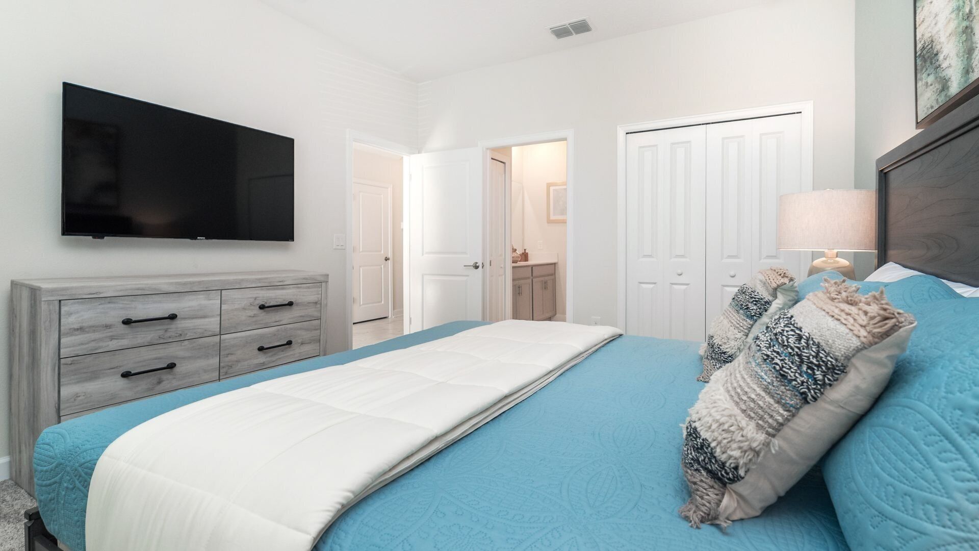 A bedroom with a bed, a dresser, a television, and a door leading to a bathroom.