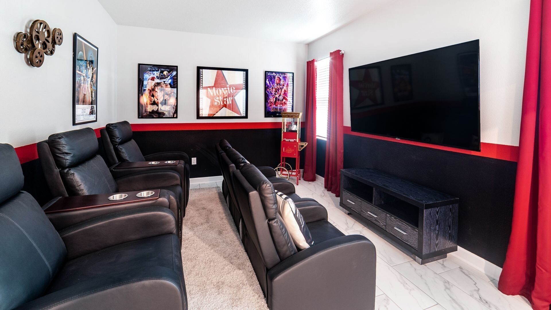 A home theater room with black leather recliners, a large flat-screen TV, and movie posters on the wall.