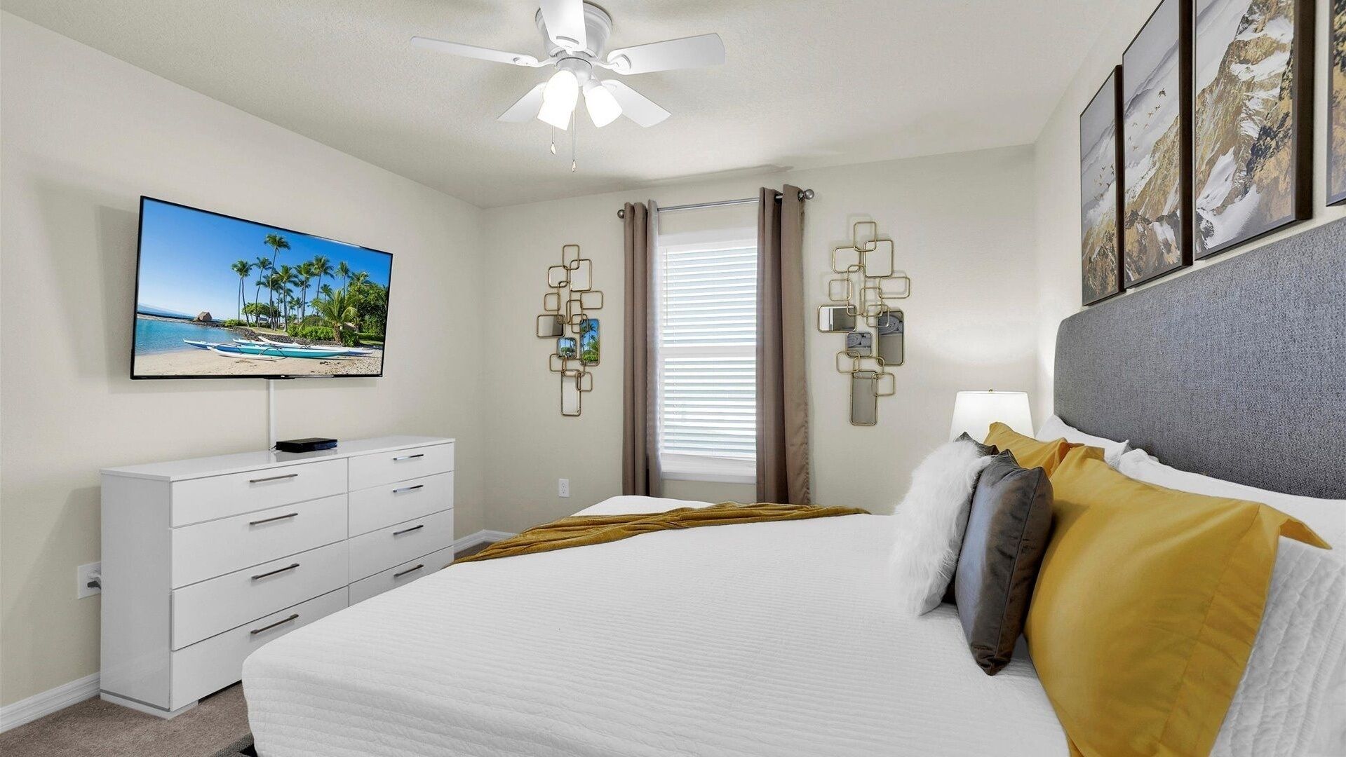 Un dormitorio con cama, televisor, ventilador de techo, cómoda y decoración en la pared.