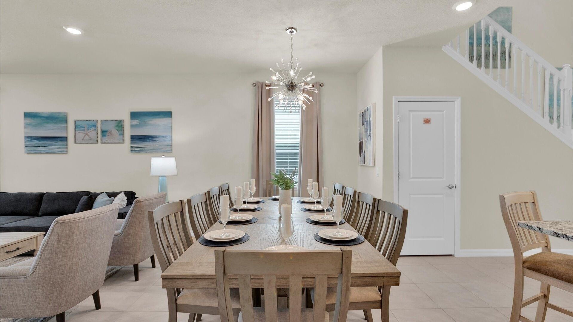 Une salle à manger avec une longue table en bois, dressée pour six personnes, flanquée de deux canapés et surmontée d’un lustre.