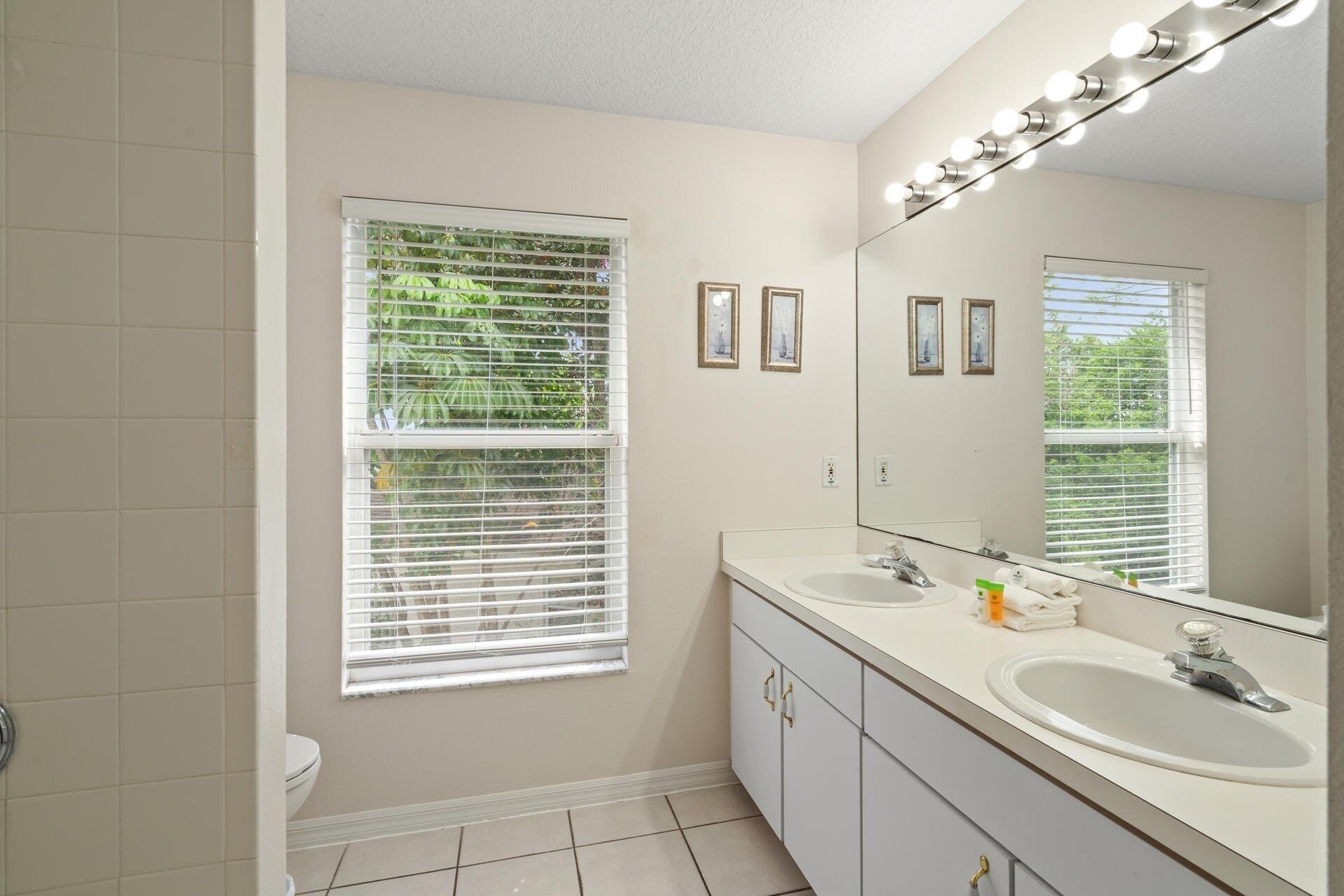 A bathroom with two sinks, a large mirror, and blinds on the windows.