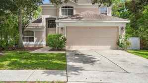 A two-story house with a beige garage door, a covered driveway, and a well-maintained lawn. - Highlands Reserve 4 Bedroom Vacation Home with Private Pool 4 Hotel Room (Davenport)