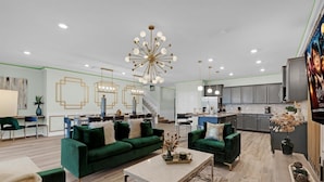 Een ruime woonkamer met groene banken, een salontafel en een moderne kroonluchter.