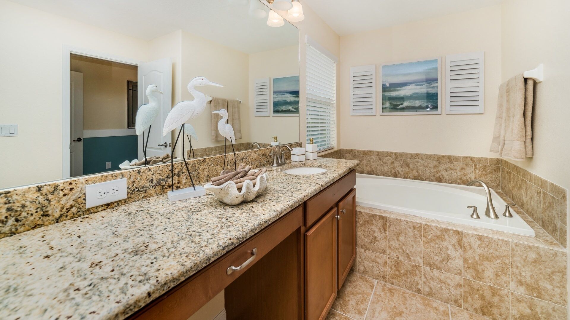 A bathroom with a granite countertop, a sink, a bathtub, and a large mirror.