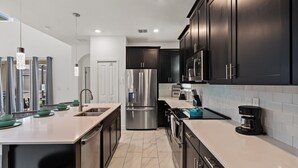 A modern kitchen with dark cabinetry, stainless steel appliances, and a light-colored countertop. - Storey Lake Resort 5 Bedroom Private Pool Home 5 Home (Kissimmee)