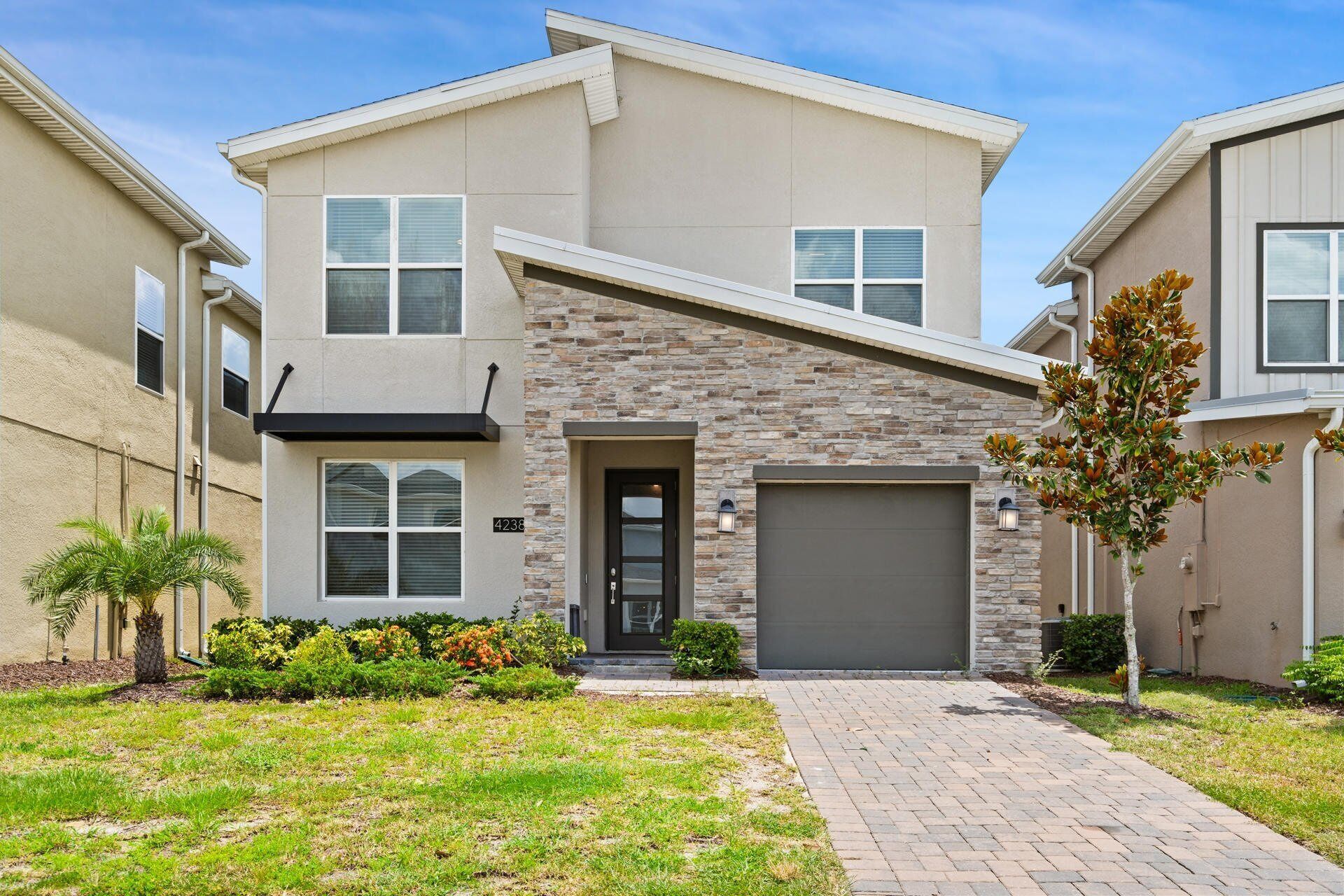 A modern two-story house with a stone facade, a garage, and a well-maintained front yard with plants and a paved walkway.