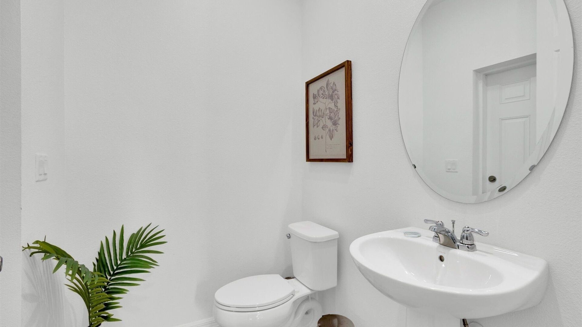 Un baño con inodoro, lavamanos e ilustración botánica enmarcada en la pared.
