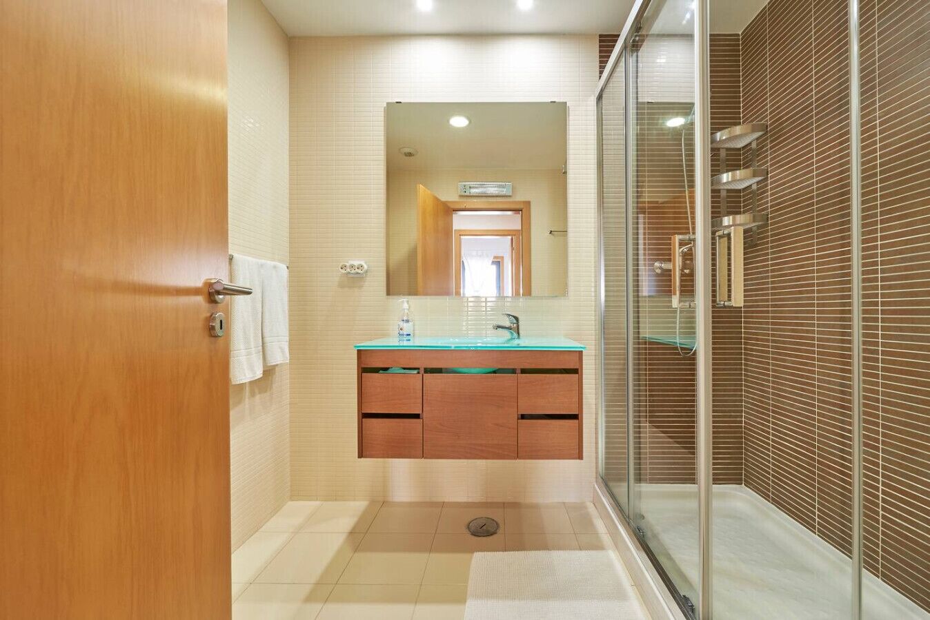 Une salle de bain moderne avec une porte en bois, une douche en verre et un meuble-lavabo surmonté d’un miroir.