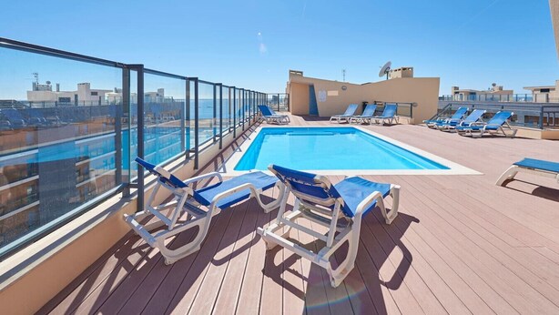 Zona de piscina en la azotea con sillones reclinables azules y una vista despejada del horizonte urbano.