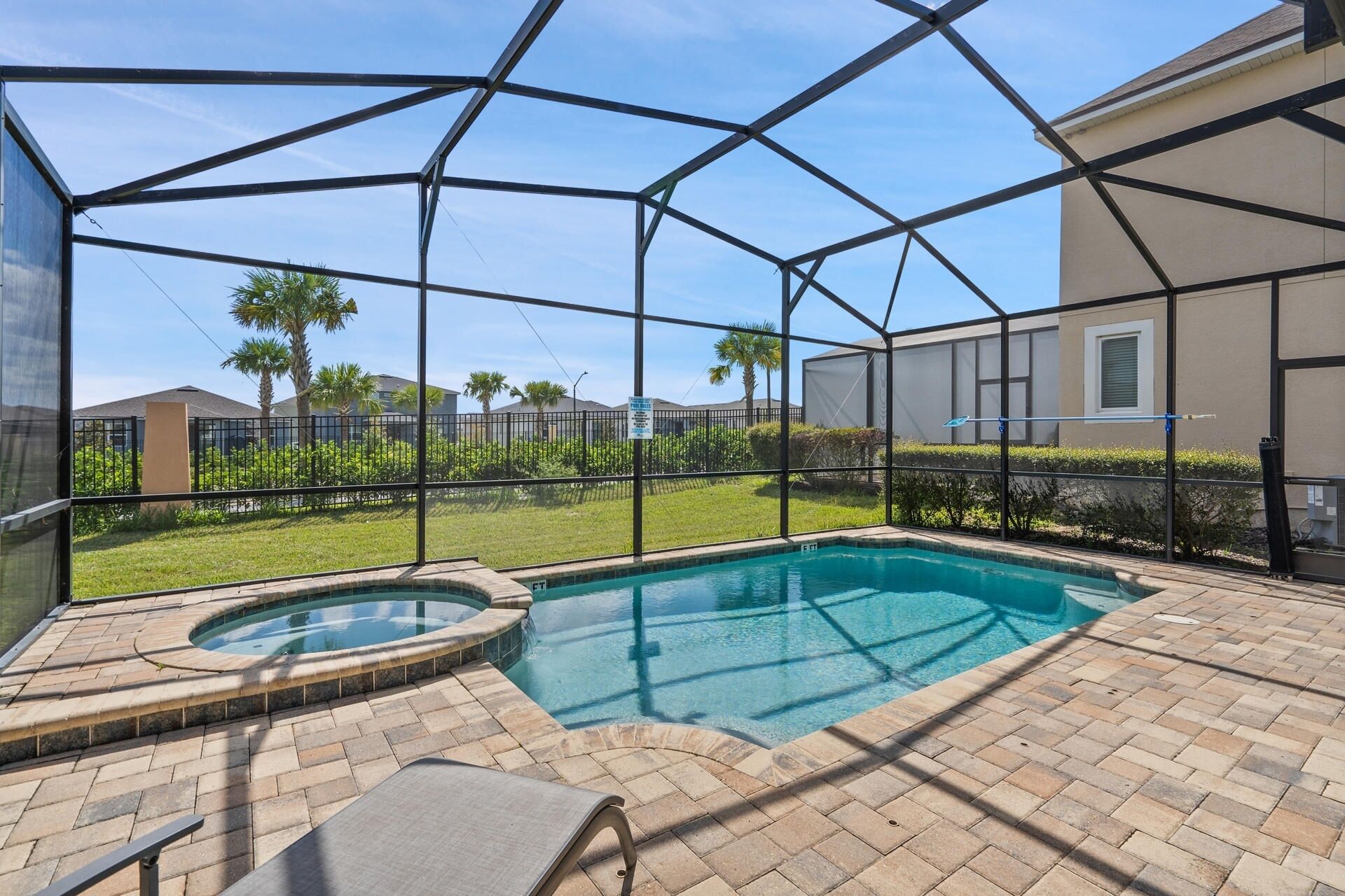 A covered outdoor swimming pool with a hot tub, surrounded by a metal fence and a brick patio.