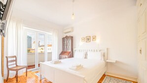 Un dormitorio con una cama grande, una silla de madera, un armario y vistas de la ciudad a través de una puerta corredera.