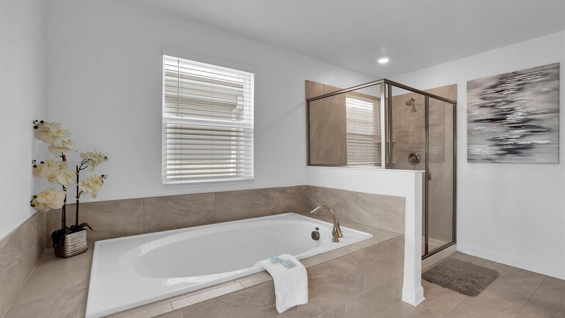 A modern bathroom with a large bathtub, a glass shower enclosure, and a window with blinds.