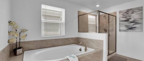 A modern bathroom with a large bathtub, a glass shower enclosure, and a window with blinds.