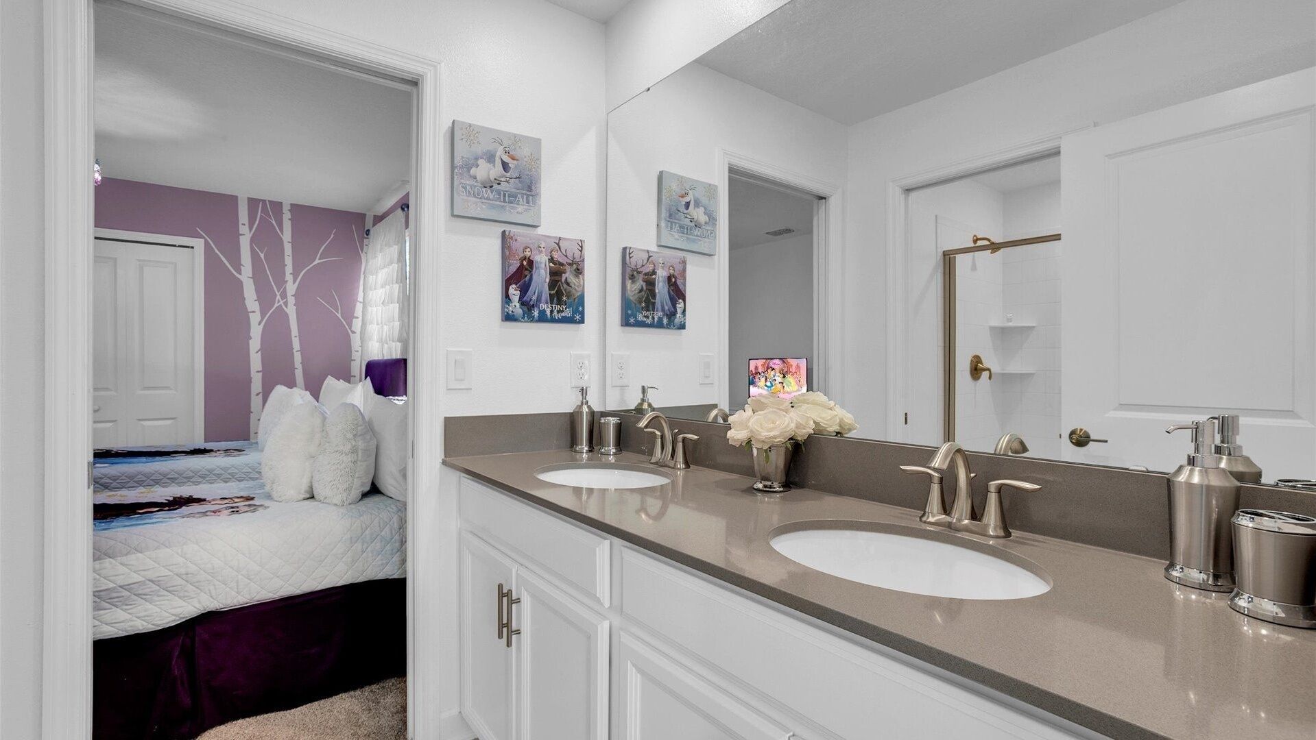 A bathroom with two sinks, a large mirror, and a bed with a purple wall and white bedding.