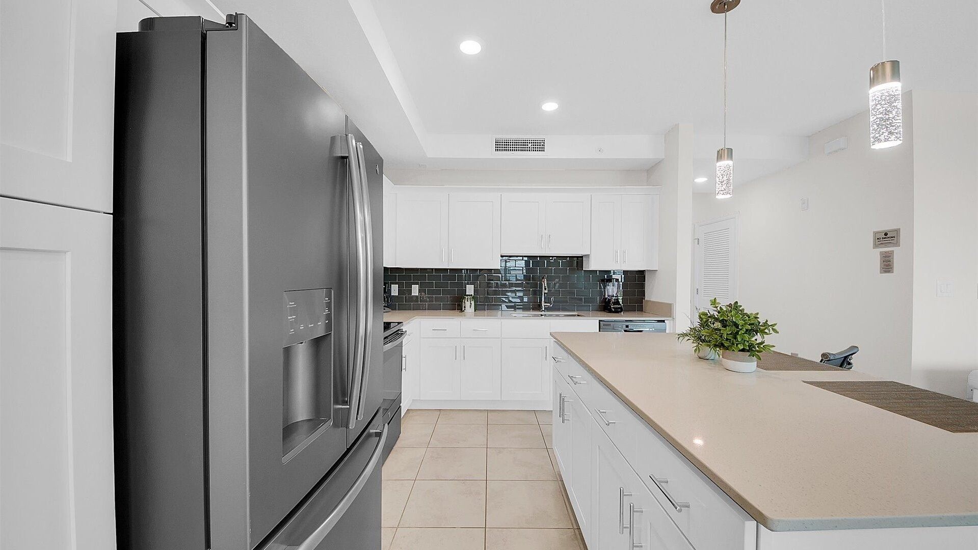 Una cucina moderna con frigorifero in acciaio inossidabile, mobili bianchi, una parete di fondo nera e un piano di lavoro color beige.