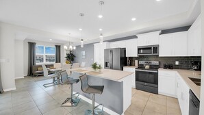 A modern kitchen with white cabinets, stainless steel appliances, and a central island with bar stools. - Storey Lake Resort 2 Bedroom Condo w Balcony and Amenities 2 Condo (Kissimmee)
