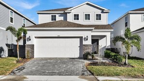 A two-story residential house with a white garage door, a brick driveway, and a stone foundation. - Windsor Island Resort 5 Bedroom Private Pool Home 5 Home (Davenport)
