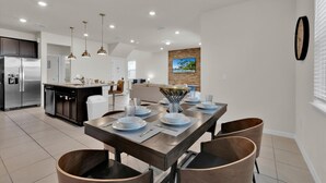 A modern kitchen with a stainless steel refrigerator, a dining area with a wooden table set for four, and a living area with a sofa and a TV mounted on the wall. - Windsor Island Resort 5 Bedroom Home Private Pool 5 Home (Davenport)
