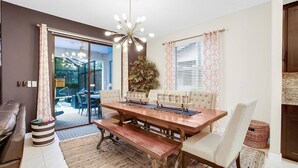 Un coin repas avec une table en bois, des chaises rembourrées et un banc. On y trouve une grande plante en pot et un lustre au-dessus de la table.