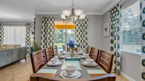 Zona pranzo con tavolo apparecchiato per quattro persone, circondata da tende decorate, un lampadario e vista sul verde.