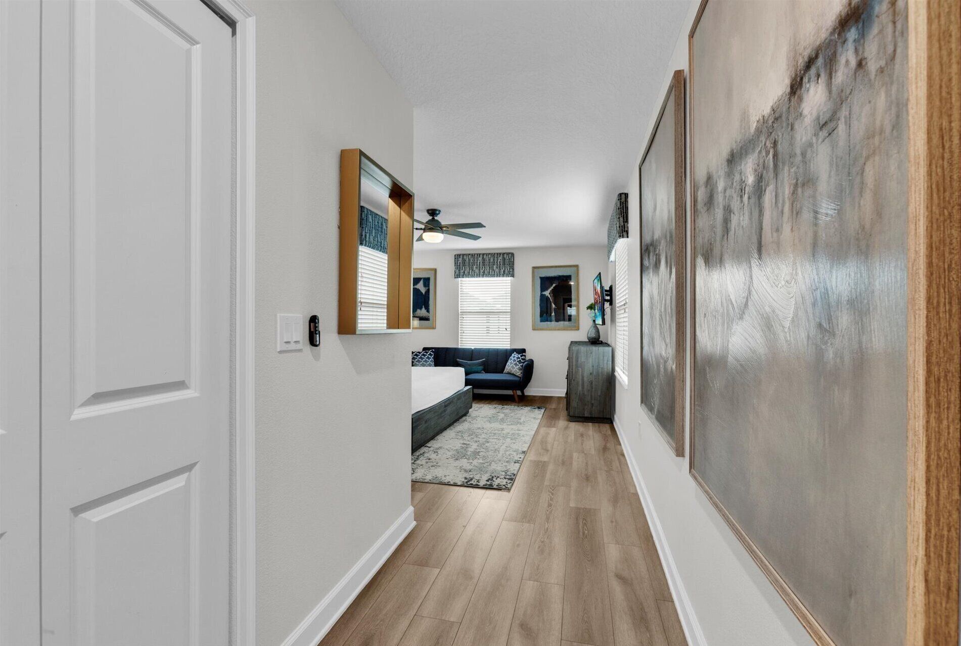 Un couloir doté d’un plancher en bois, d’un canapé de couleur sombre, d’un petit tapis et d’un grand tableau abstrait accroché au mur de droite.