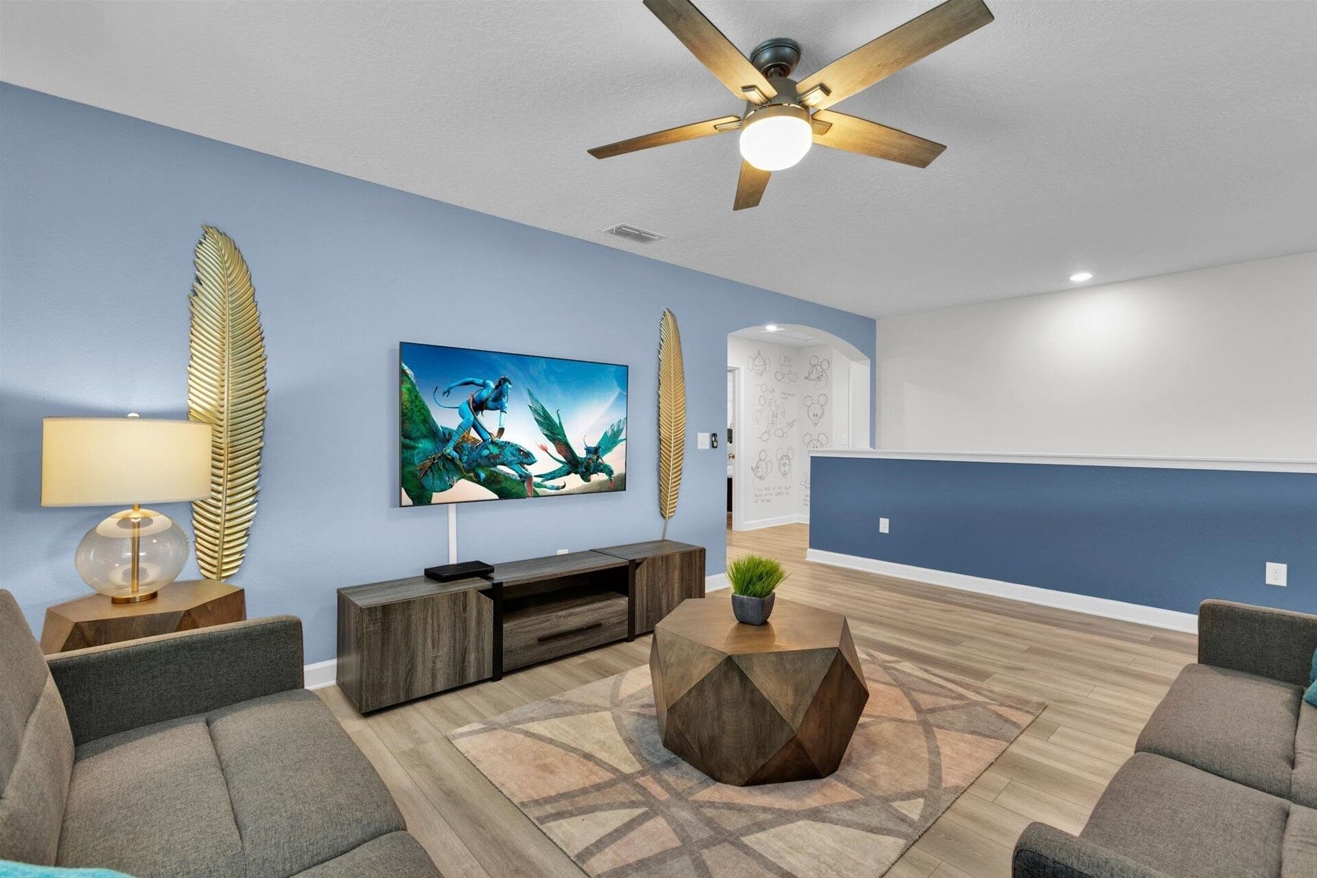 A modern living room with a blue accent wall, a ceiling fan, a large artwork, and a geometric rug.