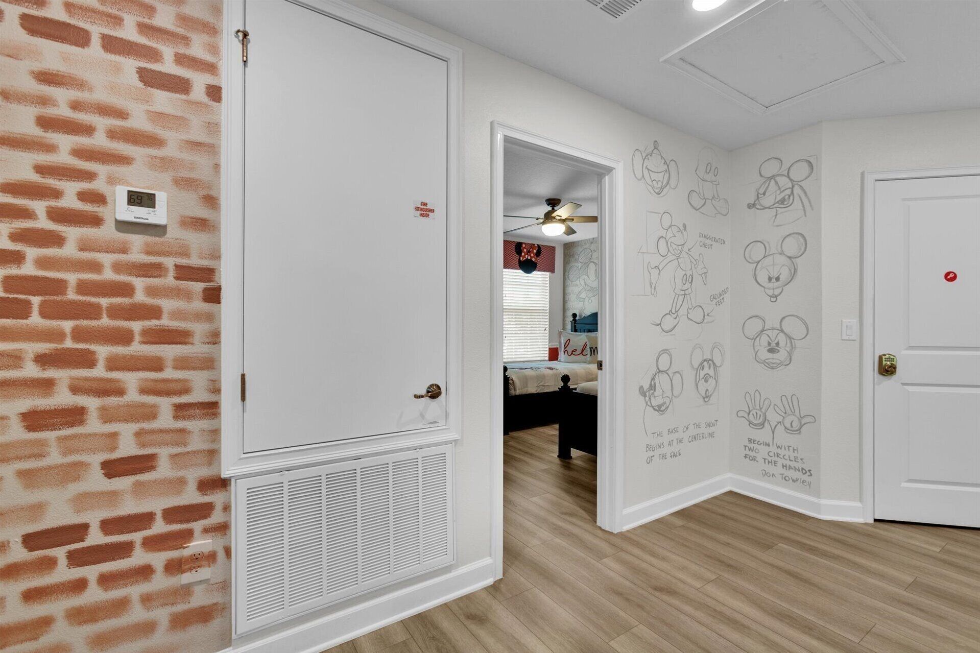 A room with a brick-patterned wall, a white door, and a wall with Mickey Mouse sketches.