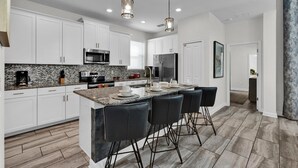 A modern kitchen with white cabinets, a granite countertop, stainless steel appliances, and a bar area with black chairs. - Storey Lake Resort 5 Bedroom Pool Home with Themed Rooms 5 Home (Kissimmee)