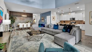 A modern living room with a sectional sofa, a coffee table, and a dining area with a white table and chairs. - Storey Lake Resort 5 Bedroom Pool Home with Themed Rooms 5 Home (Kissimmee)