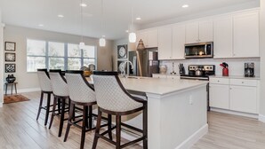 A modern kitchen with white cabinets, a central island, bar stools, stainless steel appliances, and pendant lighting. - Solterra Resort 9 Bedroom Private Pool Home Sleeps 24 9 Home (Davenport)
