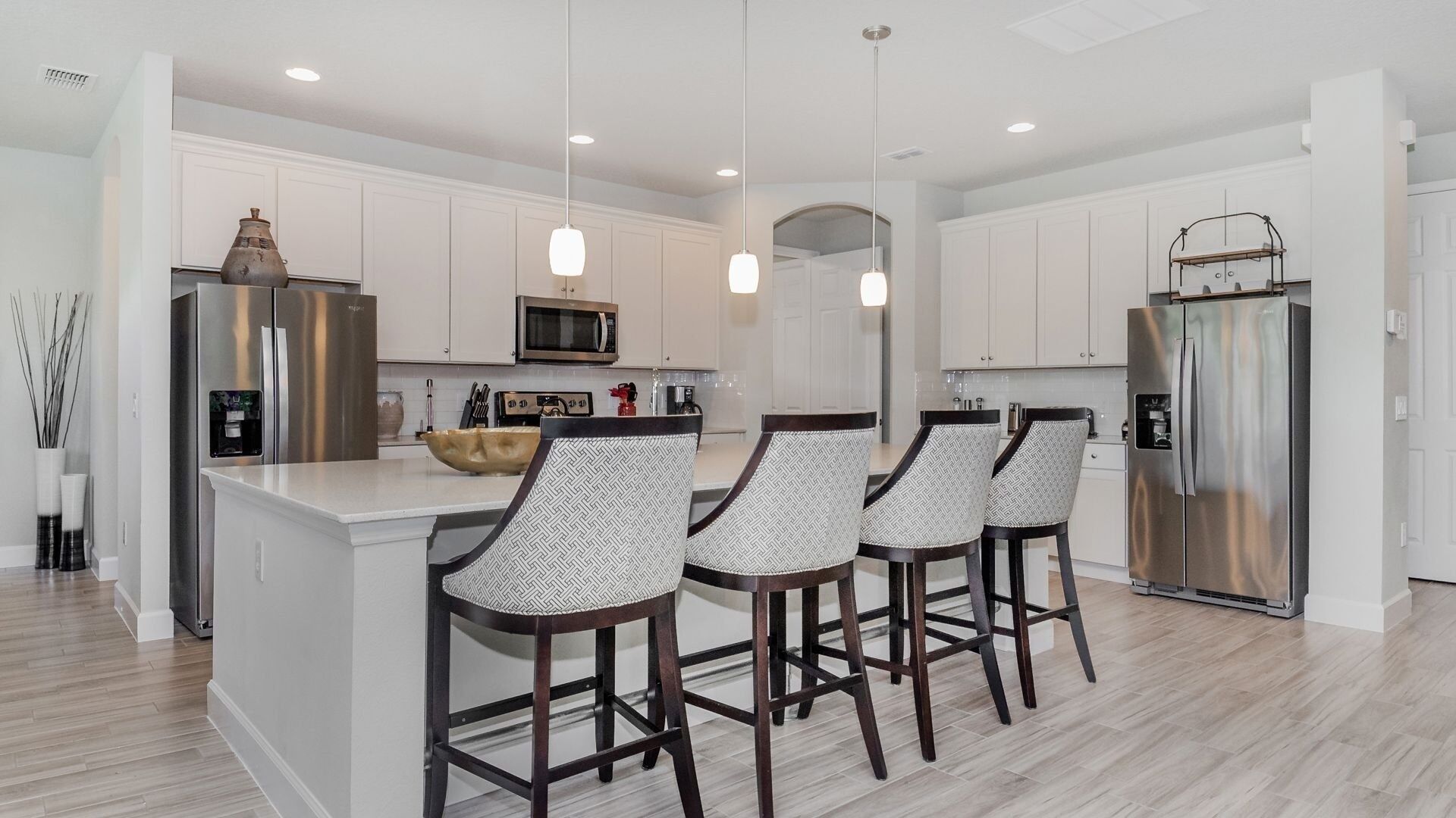A modern kitchen with white cabinetry, stainless steel appliances, and a central island with bar stools.