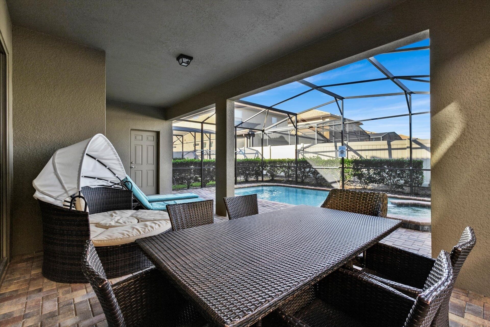 A covered outdoor area with a pool, wicker furniture, and a view of a residential neighborhood.