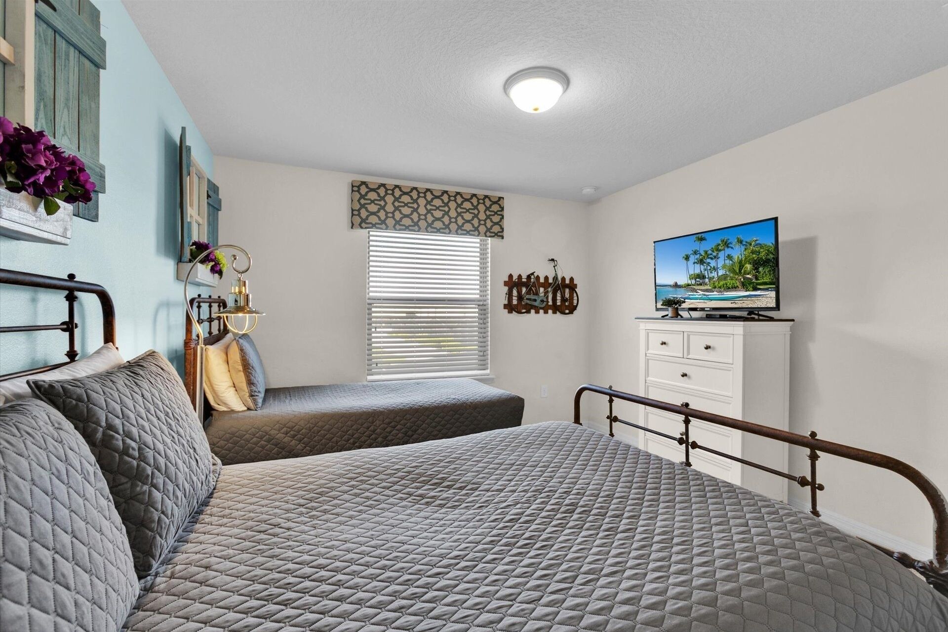 Une chambre à coucher avec un lit, une télévision, une commode et une fenêtre avec des stores.